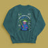 A holiday sweatshirt featuring a cute Grim Reaper holding a scythe, wearing a Santa hat. Above the character is the text "Grave Tidings We Bring," surrounded by festive snowflakes and holiday-themed designs. The combination of spooky and festive elements adds a humorous twist to traditional holiday attire.